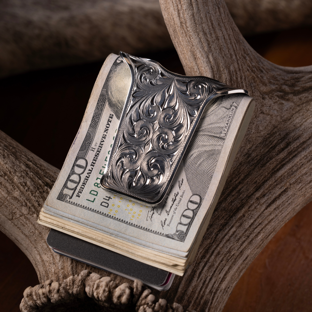 Clint Orms San Augustine sterling silver money clip holding folded bills, resting on a deer antler