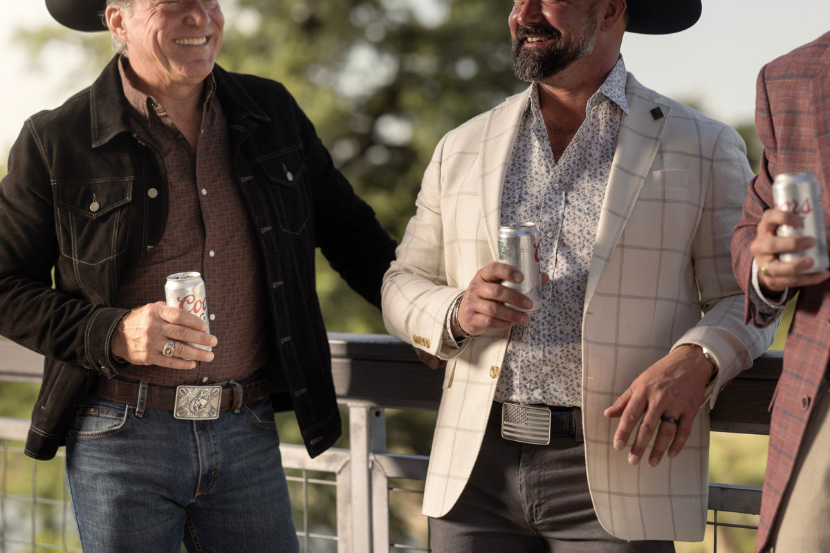 Two men in western jackets wearing Clint Orms sterling silver buckles and engraved cuffs outdoors
