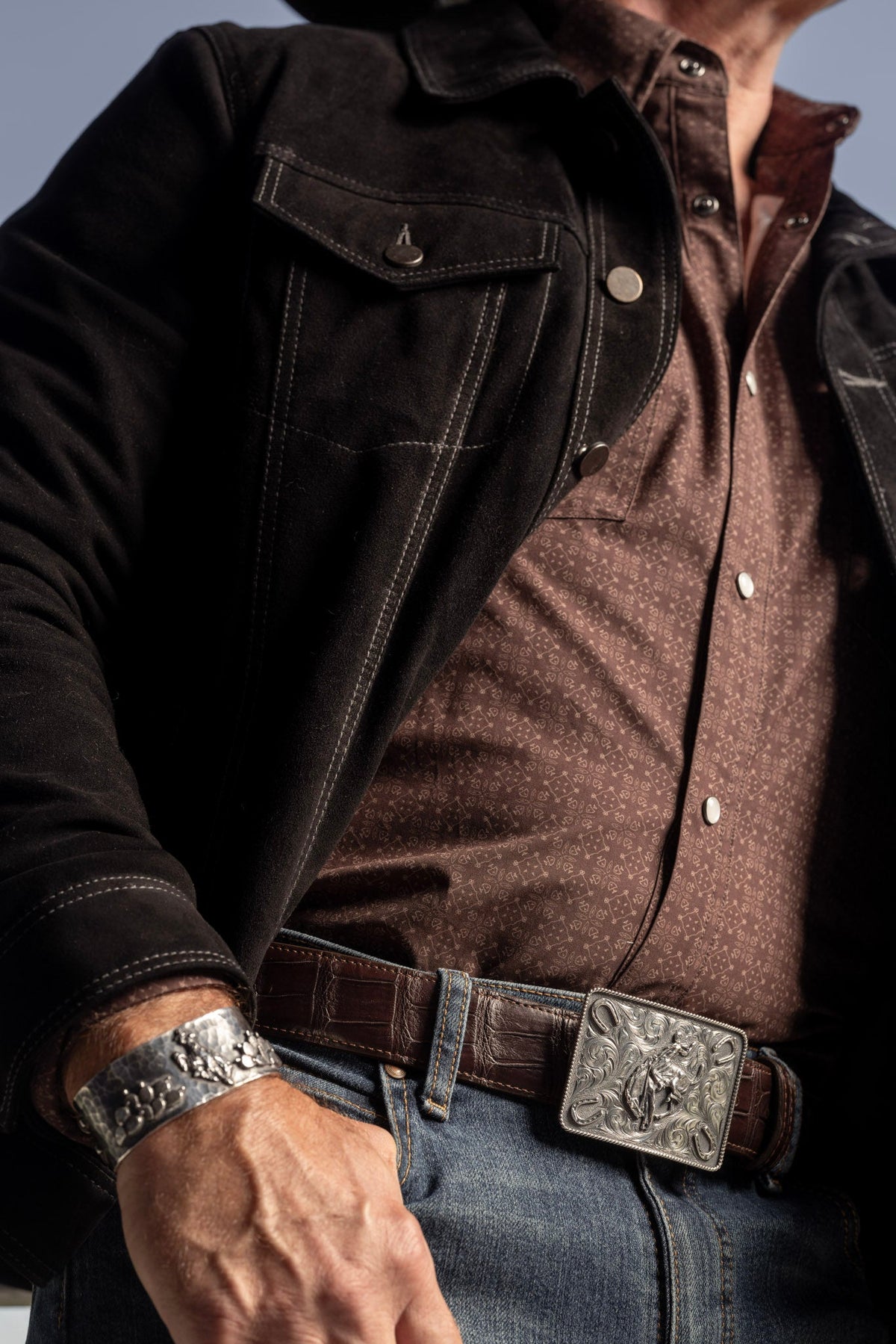 Man in a brown jacket wearing the Clint Orms Dimmit 1802 sterling silver bronc rider buckle