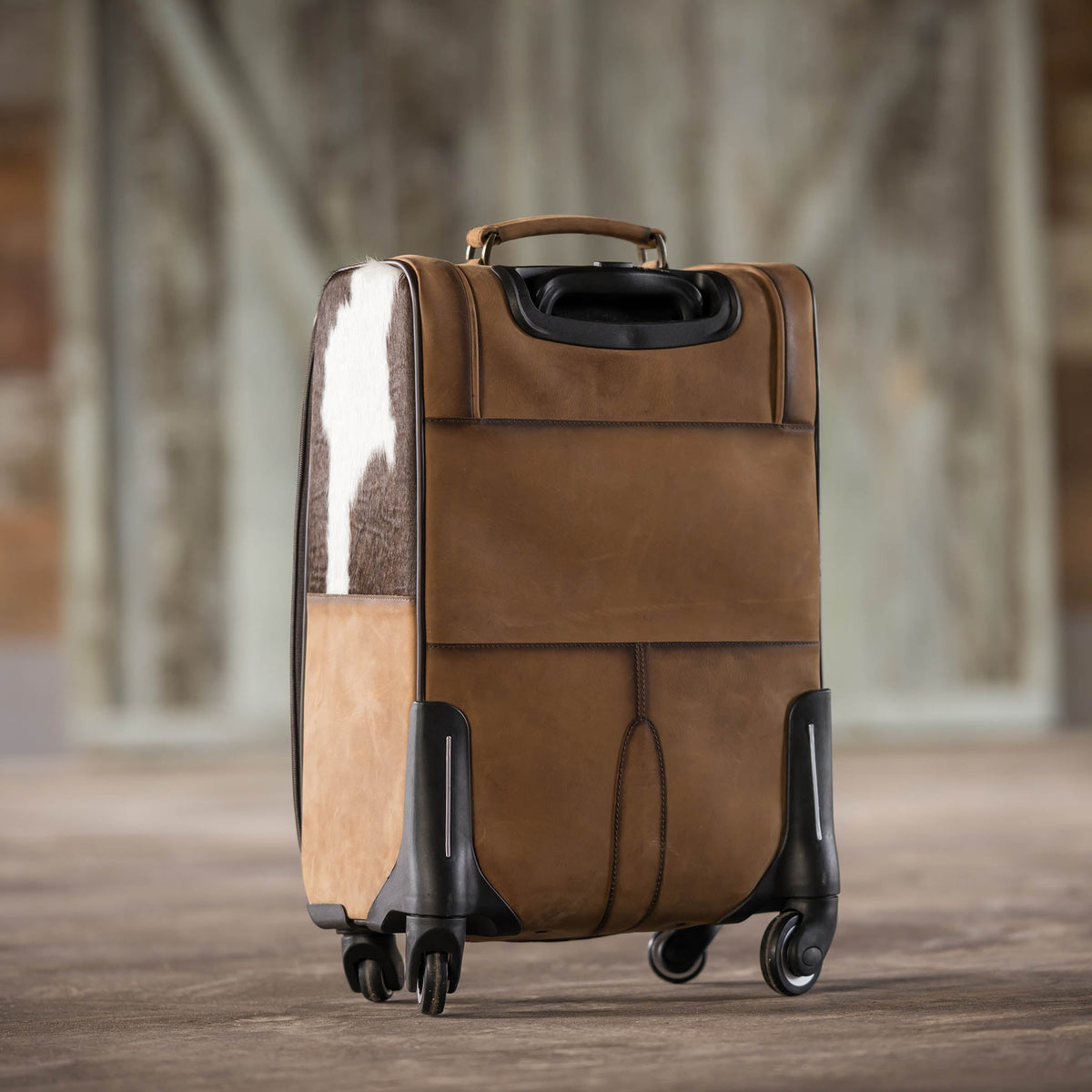 Cowhide rolling suitcase by STS Ranchwear featuring rugged leather exterior and sturdy wheels for travel.