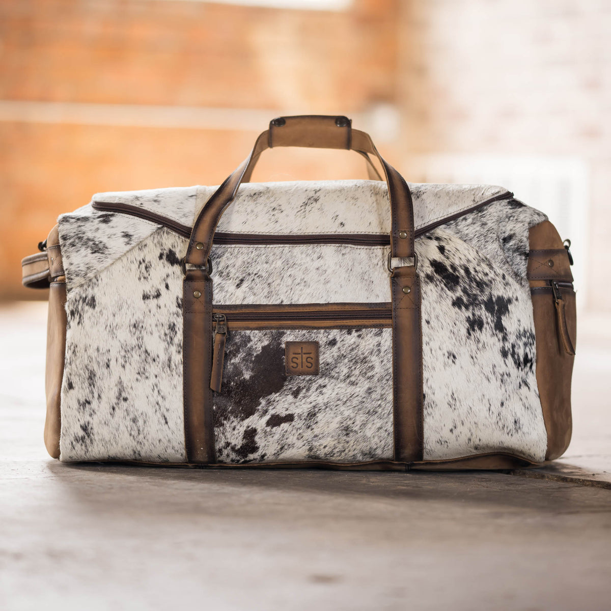 Brown cowhide Rustler Duffle bag by STS Ranchwear featuring rugged leather and spacious design for travel or outdoor use.