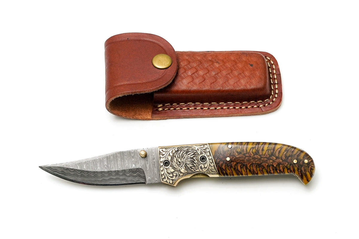 Titan International K Damascus Steel Clip Point Folding Knife with hand-engraved eagle bolster and amber pine cone handle.