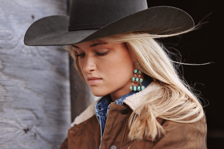 Woman in a black felt cowboy hat, turquoise earrings and a brown suede jacket
