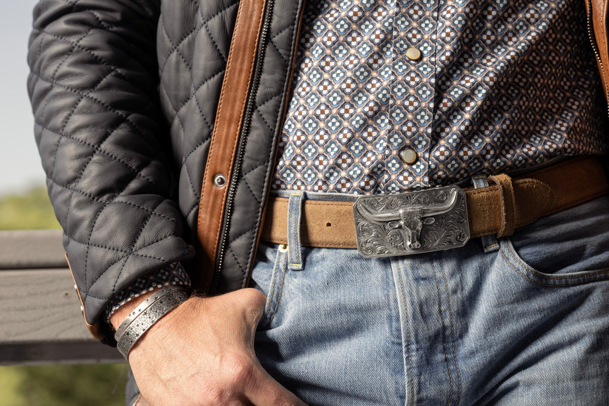 Man in a quilted jacket and jeans wearing the Clint Orms Kenedy 1819 sterling silver longhorn buckle