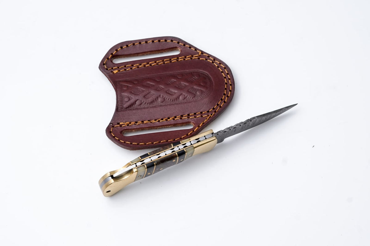 Titan International K brass and bone Damascus folding knife with leather sheath, showcasing intricate blade design and traditional craftsmanship.