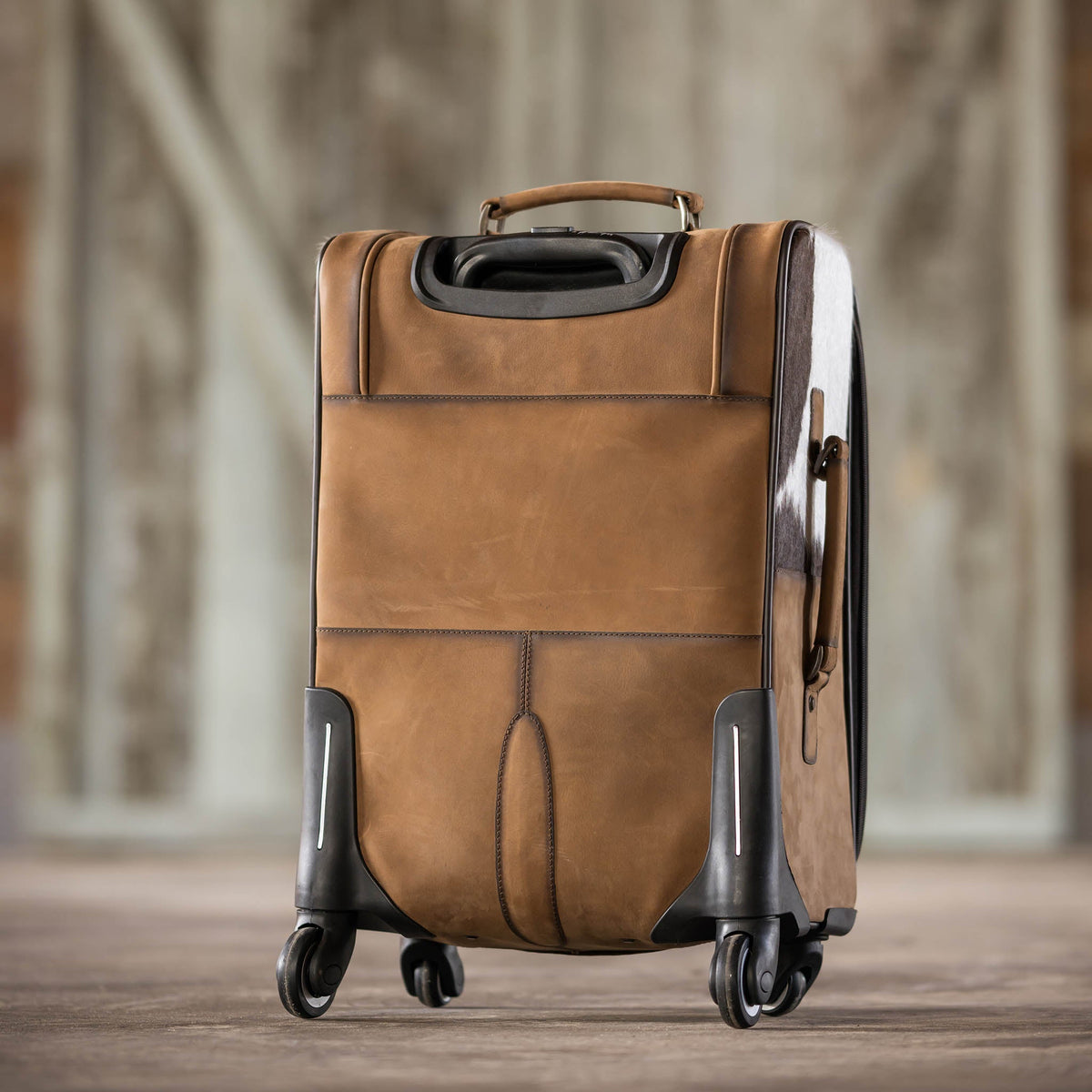 Cowhide rolling suitcase by STS Ranchwear with durable wheels and leather handle, showcasing its rustic cowhide design and craftsmanship.