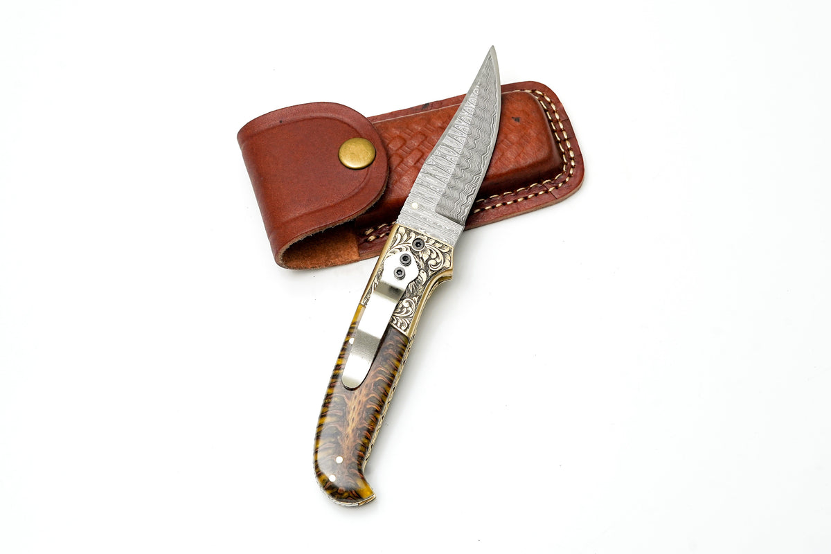 Titan International K Damascus Steel Clip Point Folding Knife with hand-engraved eagle bolster and amber pine cone handle.