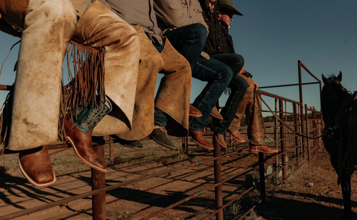 Cowboys in Justin boots sitting on a corral rail