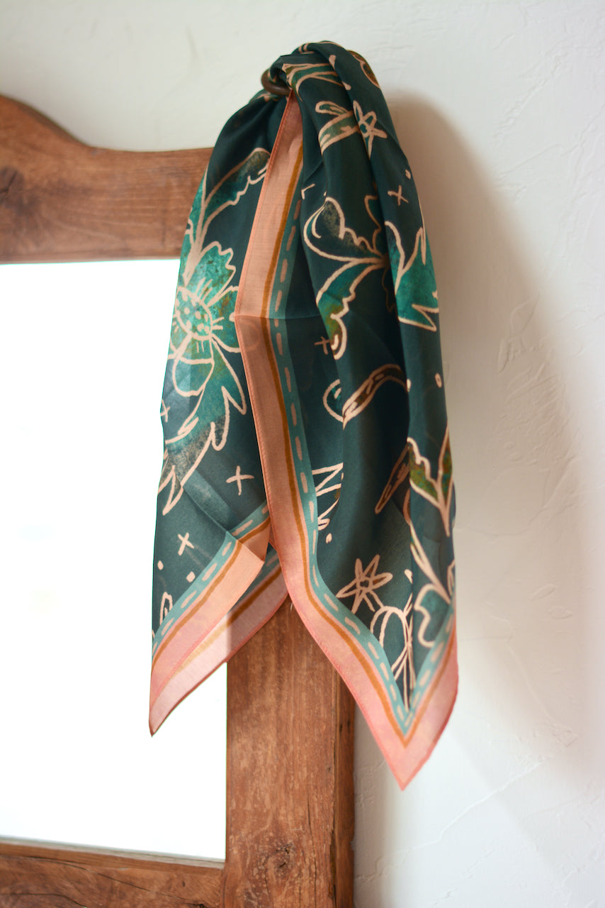 Tirzah Lane Art western silk wild rag scarf with floral turquoise and peach pattern, paired with spurs on a cowboy hat.